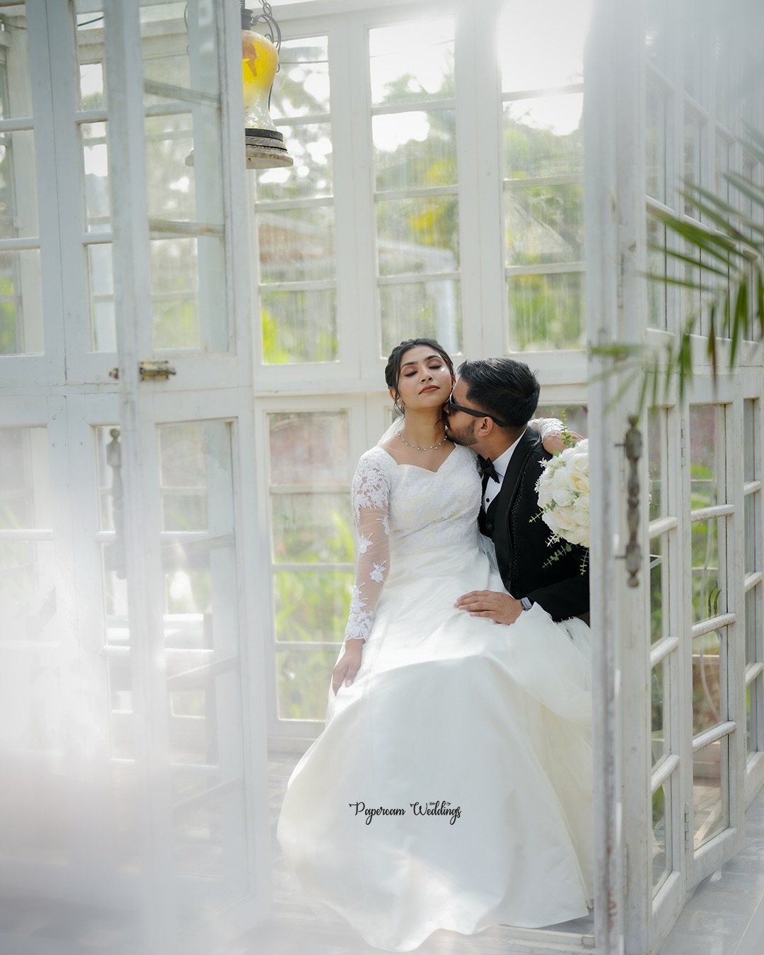 Newlyweds sharing a quiet moment inside a sunlit glasshouse